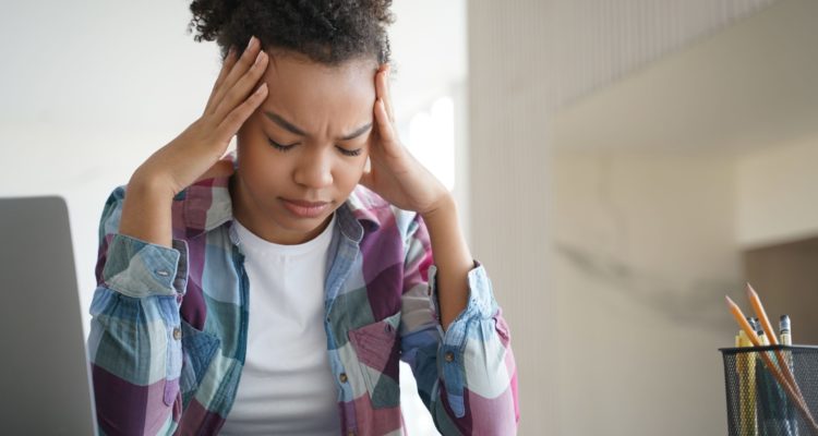 Tired african american teen girl suffer headache doing homework at laptop. Difficult elearning