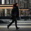 a person confidently strides down a city street, wearing a sleek black jacket that flutters slightly in the breeze.
